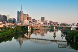 Scenic view of Nashville skyline and pedestrian bridge reflecting in the Cumberland River at sunrise.
